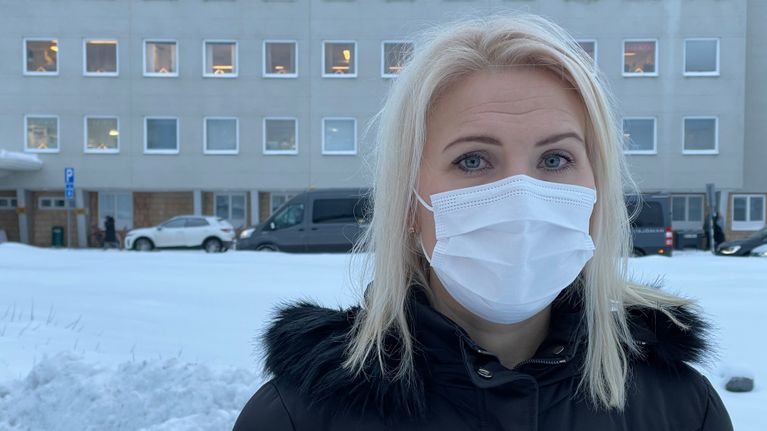 Kvinna i munskydd utomhus framför sjukhus.