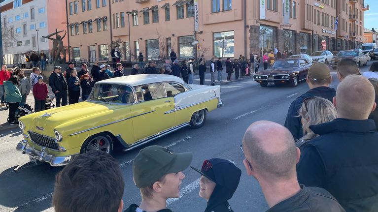 Amerikanautot ajavat Vaasan keskustan läpi vappuna. Suuri määrä ihmisiä katselee ympärillä.