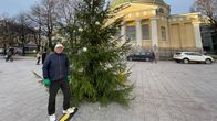 Joulukuusi keltaisen, pyöreän kirkkorakennuksen edustalla, torin laidalla. Henkilö seisoo havupuun edessä 