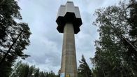 Betonisen vesitornin takana on tummia pilviä ja vieressä mäntymetsää.