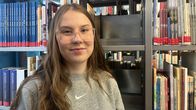 Senja Aikio seisoo kirjastossa kirjahyllyn vieressä. 