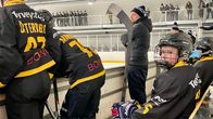 Juniorikiekkoiijat istuvat vaihtopenkillä jäähallissa.