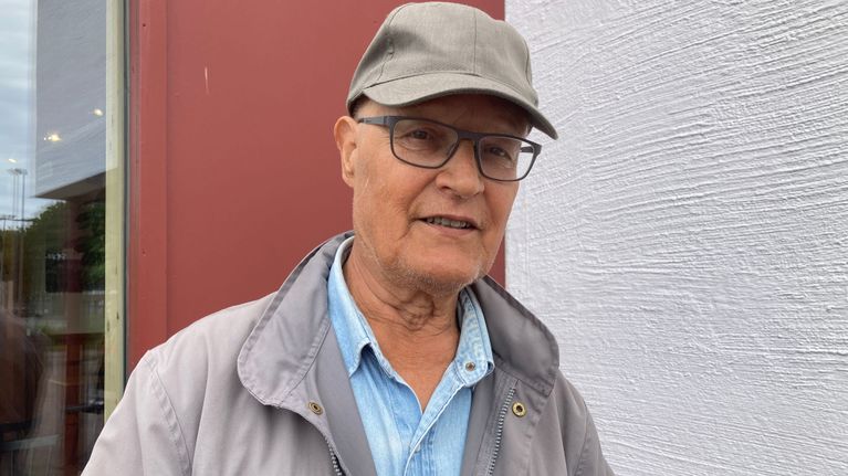Lippalakkipäinen iäkäs mies katsoo kameraan.