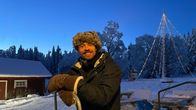 Mies seisoo karvahattu päässä keskellä lumista pihaa. 