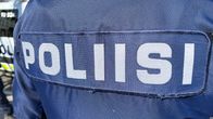 Sinisen haalarin selkä, jossa lukee "poliisi". Taustalla näkyy hieman poliisiautoa.