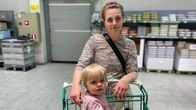 Lapsi istuu ostoskärryissä ja katsoo kameraan, lyhyttukkainen äiti kirjavassa mekossaan nojaa kevyesti ostoskärryyn. Takana oikealla on isoja kananmunalaatikoita ja kananmunakennoja hyllyillä.