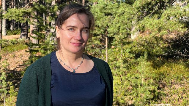 Nainen seisoo havumetsässä aurinkoisella säällä, taustalla näkyy puita ja metsänpohjaa 8.10.2026 Inarissa. 