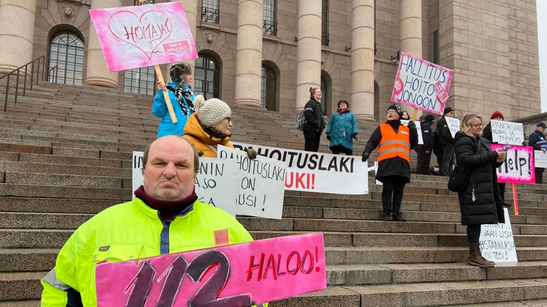 Ryhmä ihmisiä osoittamassa mieltä parlamenttitalon portailla.
