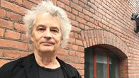 Harmaatukkainen mies seisoo kuvan vasemmassa laidassa, taustalla tiiliseinä. Kuvassa on Eppu Normaali-yhtyeen Juha Torvinen.