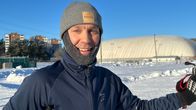 Mies hymyilee ulkoiluasussa talvella. Taustalla on halli.