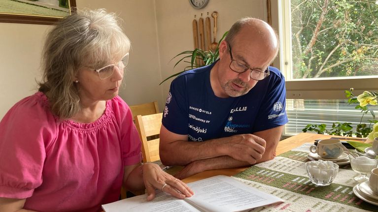 Nainen ja mies istuvat pöydän ääressä ja lukevat kirjaa.