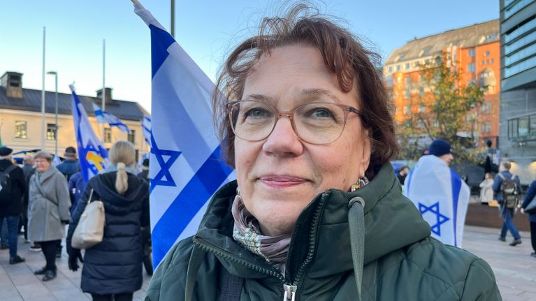 Henkilö kuvattuna edestä. Taustalla mielenoisoittajia Israelin lippujen kanssa.