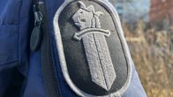 Tummansävyinen poliisin hihamerkki. Miekka, jolla on leijonan pää. 