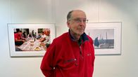 Punaiseen fleece-paitaan pukeutunut mies seisoo taidenäyttelyssä valokuvateosten edessä.