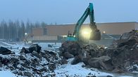 Etualalla kaksi kaivinkone murskatun kallion keskellä. Taka-alalla rakenteilla oleva uimahalli.