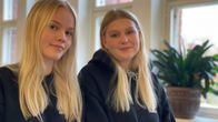 Kaksi vaaleahiuksista ja mustavaatteista nuorta naista istuu vierekkäin ja katsoo kameraan.
