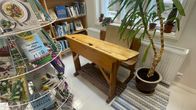 En krukväxt och en gammal pulpet från en skola står framför ett fönster i skolan, som nu är ombyggd till bibliotek och har böcker i en ställning och på hyllor.
