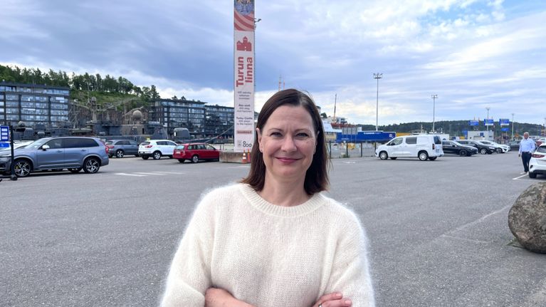 En kvinna i vit blus står med armarna kors. 