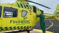 Vihreisiin haalareihin pukeutunut lentäjä liimaa tarraa keltaisen lääkärihelikopterin kylkeen