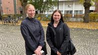 Kaksi nuorta hymyilee kameralle koulun pihalla.