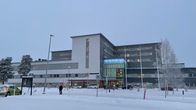 Kainuun keskussairaala lumisena päivänä, ja mustiin pukeutunut mies ylittää tien.