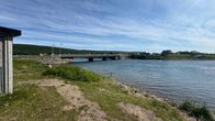 Kuvassa kesäpäivänä Vestre Jakobselv joki. Pohjois-Norjassa sijaitsevan joen yli menee silta. Taustalla taloja ja liehuvia viirejä.