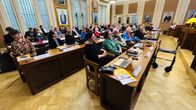Lahden kaupunginvaltuuston kokous valtuustosalissa, valtuutettuja pöytiensä ääressä. Huoneen seinillä on suuria muotokuvia.