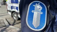 Poliisin hihamerkki, jossa miekalla on leijonan pää. Taustalla näkyy poliisiauton peräosa. 