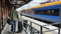 Keväisesti pukeutunut mies menee olkalaukun ja vetolaukun kanssa liuskaa pitkin junalle.
