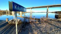 Kalkkisen kylän kyltti Kymijoen rannalla kirkkaana kevätaamuna kuvattuna.