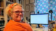 Oranssiin pukeutunut kirjailija Kaisa Viitala istuu läppäri auki edessään ja katsoon kameraan.