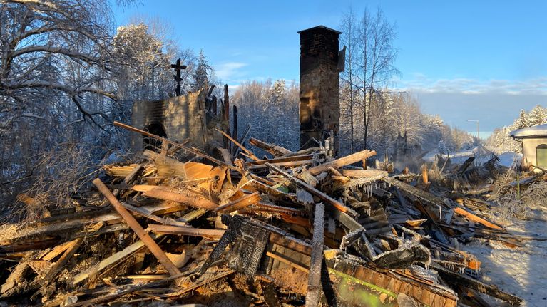 Kuvassa on tulipalon tuhoama entinen motelli. Röykkiö palaneita puita sikin sokin.