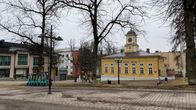 Kellertävä puurakennus, jossa torni. Edustalla nupukivikatu. 