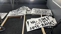 Mielenosoitusplakaatteja linja-autontavaratilassa.
