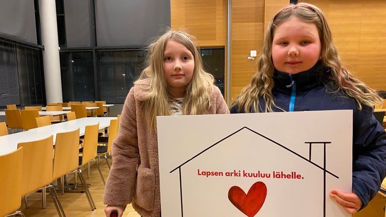 Kaksi lasta pitää kylttiä missä vedotaan oman lähikoulun puolesta, 
