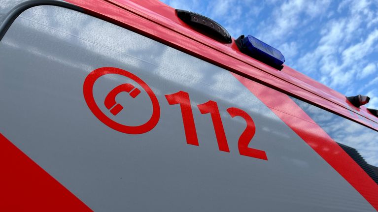 Osa auton kyljestä, jossa on punaiset ja harmaat teippaukset. Keskellä on punainen puhelinluurin kuva ja numero 112.