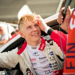 Sami Pajari smiling whilst sat in a car, with the car door open.