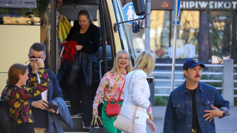 Ihmisiä astuu ulos bussista, Tytti Tuppurainen hymyilee leveästi.