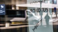 Koronarokotuspaikan lasiovesta heijastuu  ihmisen hahmo. Ikkunassa lappu, jossa lukee koronarokotus.