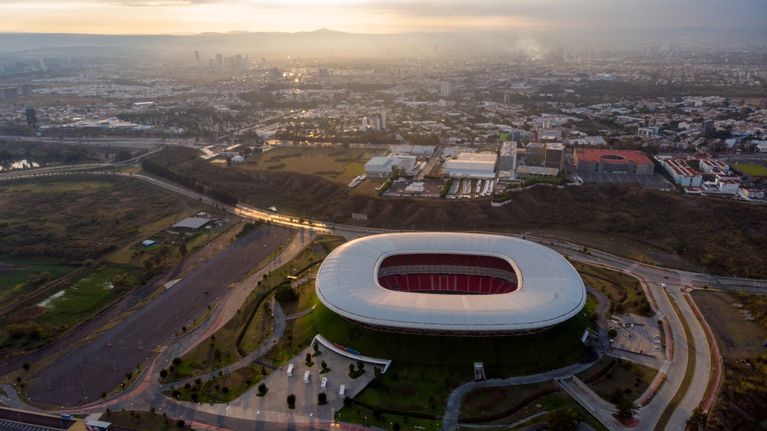Solen går ned (eller upp) bakom backarna på horisonten. I förgrunden syns stadion i Guadalajara.