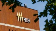 A upper corner of a red-brick building with a white sign saying HELEN, framed by leafy branches. 