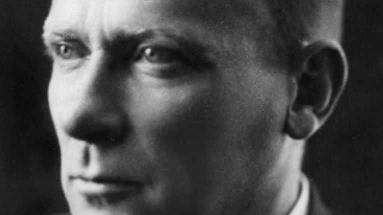 Mihail Bulgakov katsoo kuva-alalla vasempaan mustavalkoisessa kuvassa tummaa taustaa vasten.