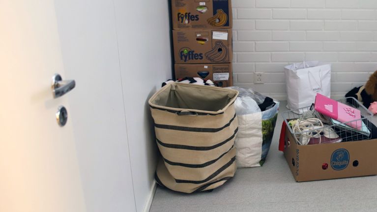 Huoneen lattialla on muuttolaatikoita ja erilaisia kasseja.