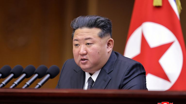 Kim Jong-Un talar med en rad mikrofoner framför sig och nordkoreanska flaggan i bakgrunden. 