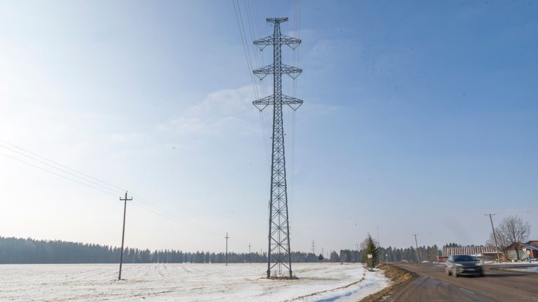 Voimalinja ja auto kevättalvisella maisematiellä pellon laidalla.