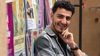 Näyttälijä Yussef Asab Alkhatib nojailee iloisena Teatterikorkekoulun ilmoitustauluun.