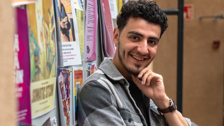 Young man in grey shirt with his arms folded, smiling as he looks into the camera.