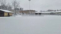Snöbeklädd isplan med ljus skolbyggnad i bakgrunden.