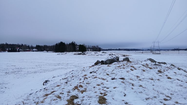 Rautakautinen röykkiö Kokemäellä pellolla lumen alla, taustalla sähkölinja.