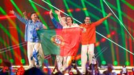 Fyra personer håller upp Portugals flagga på en scen med färgglada ljuseffekter och laserstrålar.